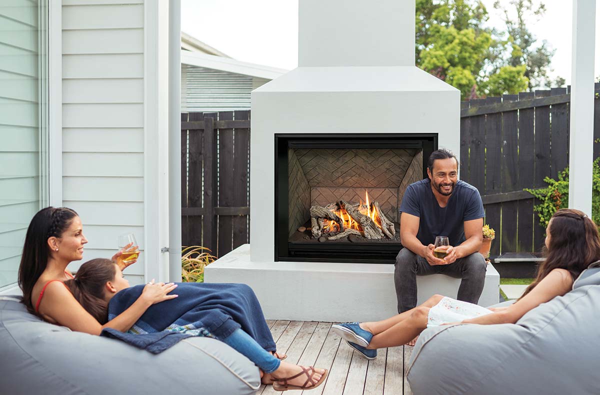 A family gathered together around the fireplace outdoors on a patio.